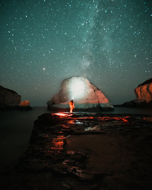 Free Person Standing on Rock Near Body of Water during Night Time Stock Photo