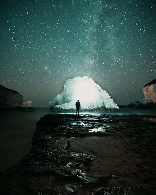 Free Person Standing on Rock Formation Near Body of Water during Night Time Stock Photo