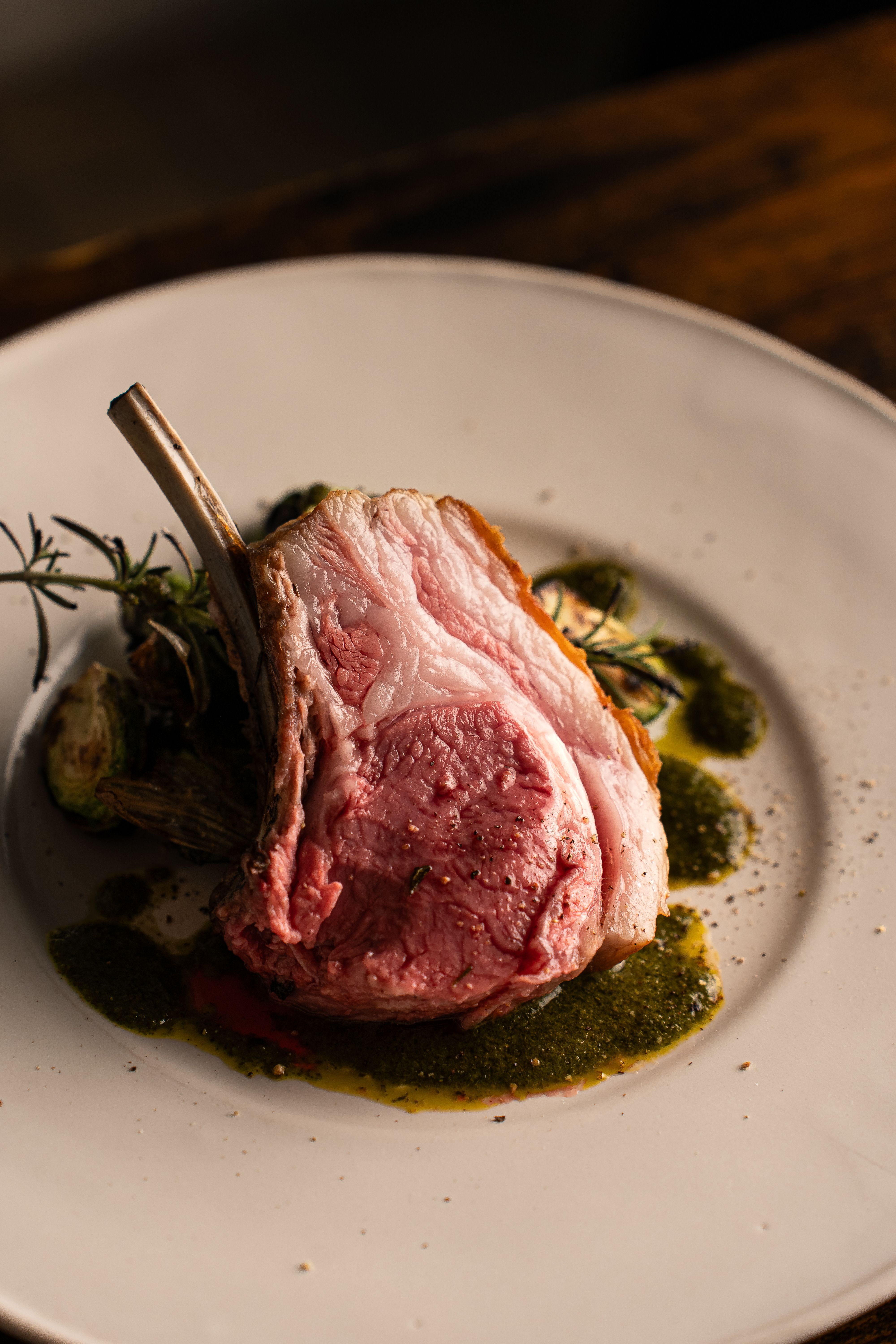 A bone-in prime rib roast with a dark herb-crusted exterior, sliced into thick rosy-pink pieces on a wooden carving board next to the rib bones.
