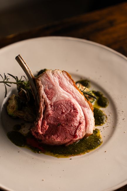 A bone-in prime rib roast with a dark herb-crusted exterior, sliced into thick rosy-pink pieces on a wooden carving board next to the rib bones.