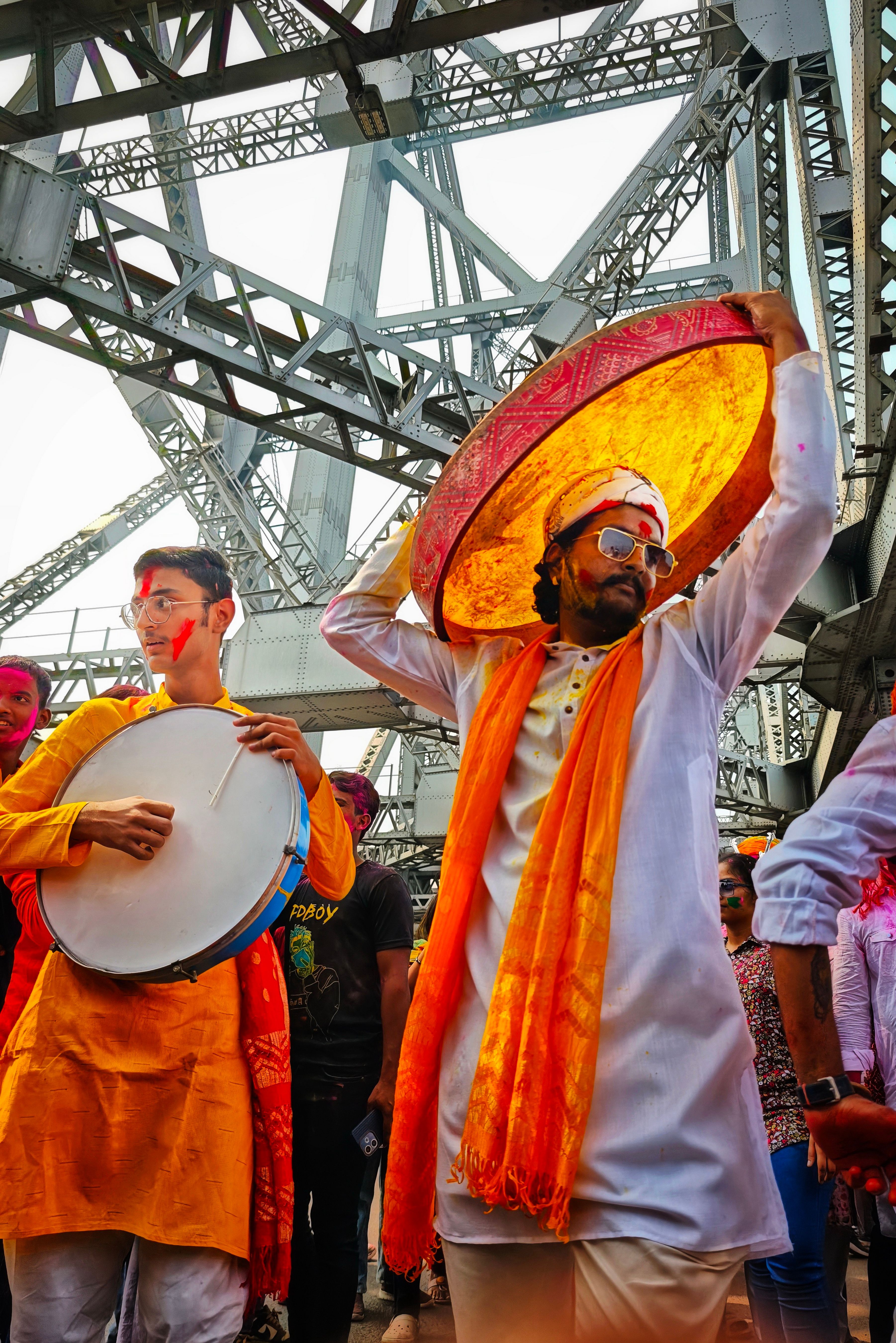 Colorful Holi festival celebration under Howrah Bridge in Kolkata, capturing traditional dance and music.