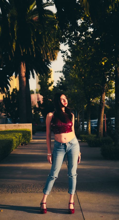 Free Stylish young woman in casual fashion posing outdoors under palm trees during golden hour. Stock Photo