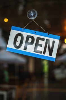 Vibrant open sign hanging on a glass storefront, welcoming customers inside.