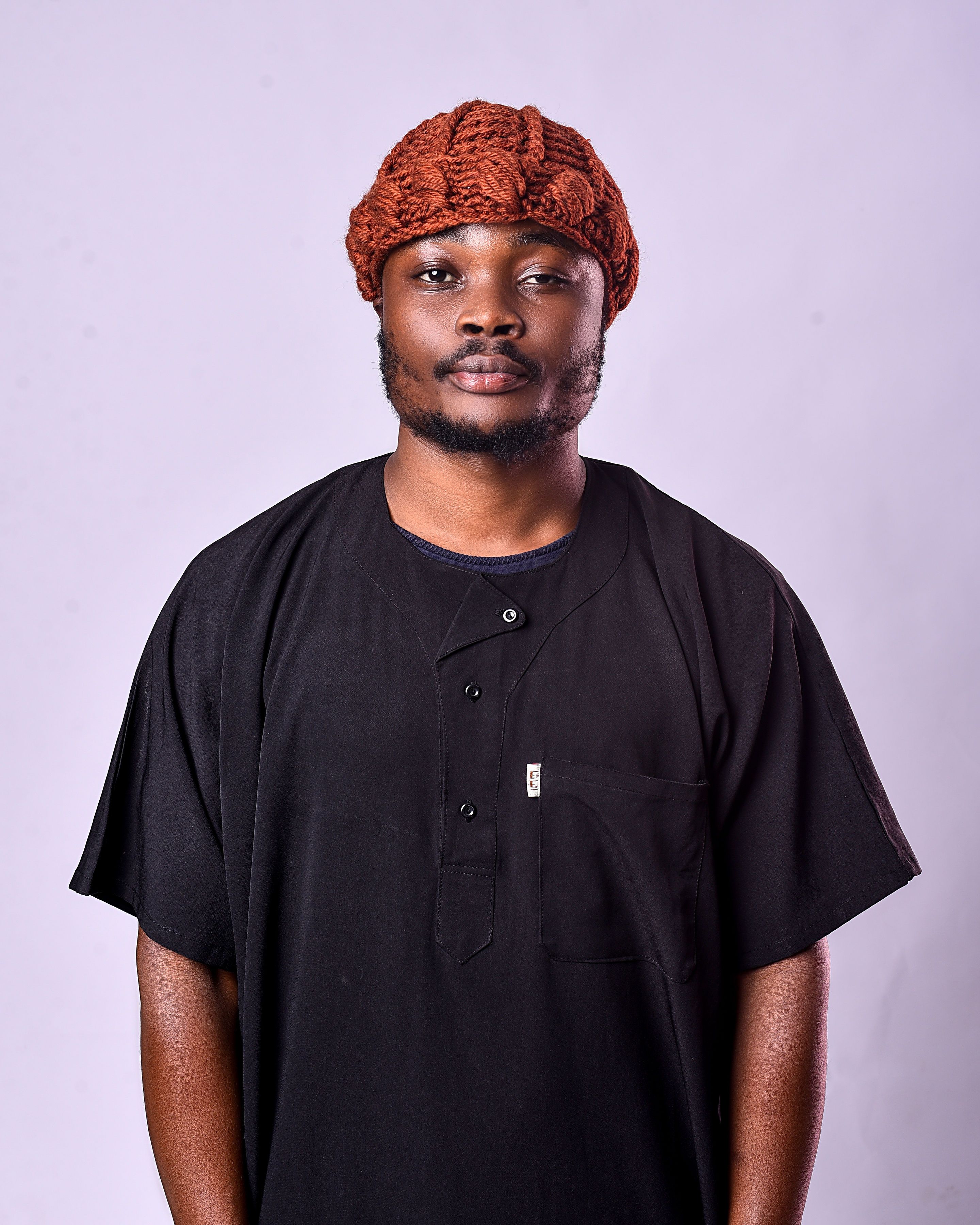 Studio portrait of an adult man wearing traditional African attire and a knit cap, with a neutral background.