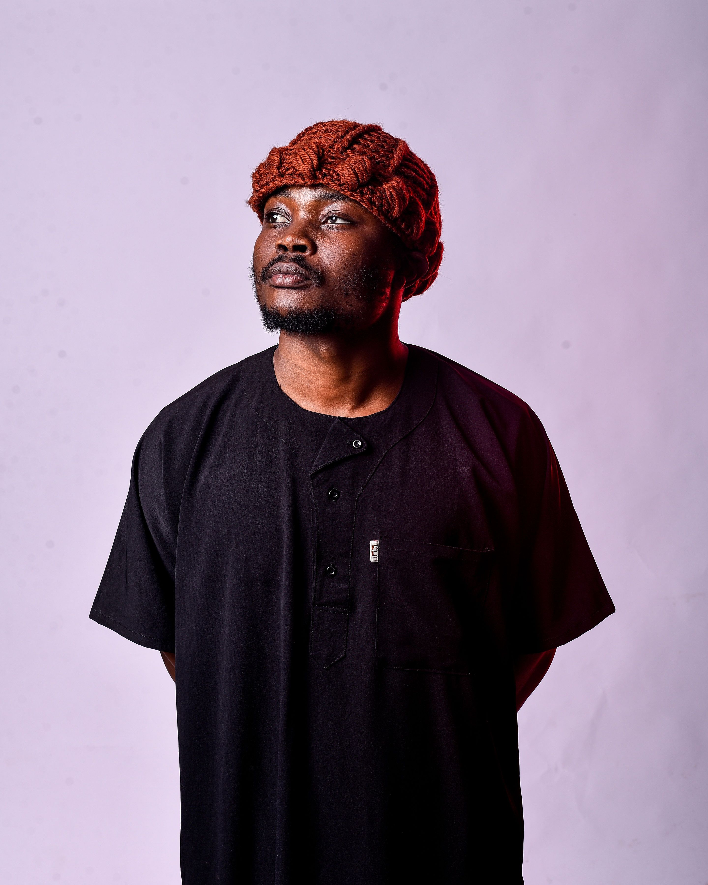 Portrait of a confident man wearing traditional attire with a head wrap, set against a studio background.