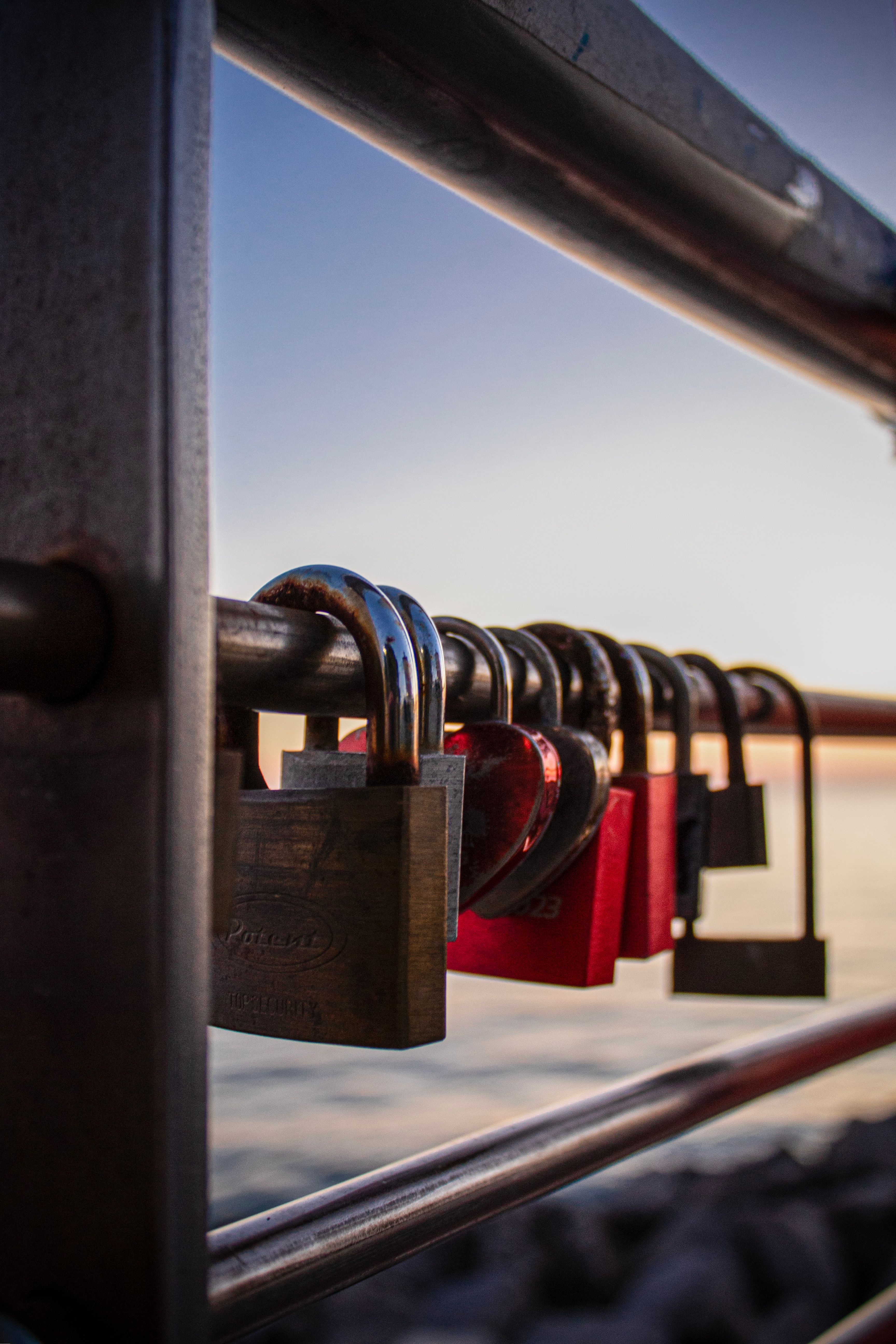 Artistic close-up of padlocks on a rail during a sunset over the ocean in Grado, Italy, capturing romance and memories.