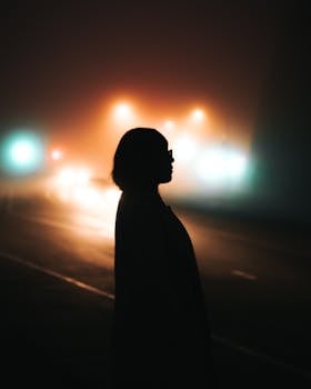 夜晚，一名女子的剪影站在雾气弥漫、路灯映照的街道上