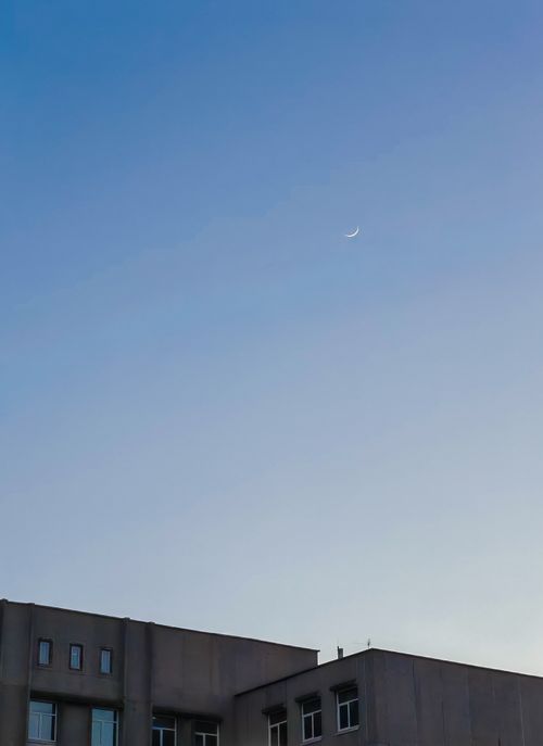 Free A serene crescent moon in the evening sky above a modern city building. Stock Photo