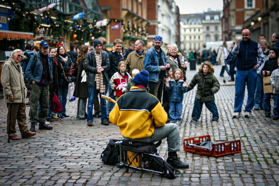 Street performer in London entertains a diverse crowd on cobblestone street.