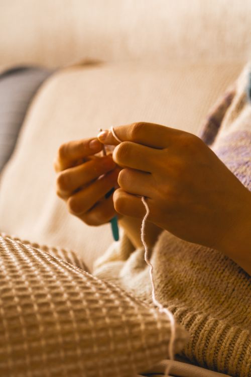 Free A warm, detailed shot of hands knitting a piece in a cozy home environment, emphasizing texture and warmth. Stock Photo