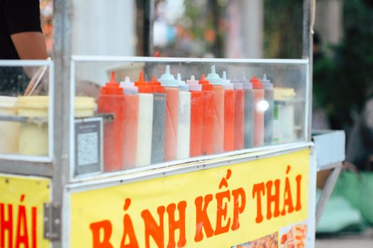 Street food cart with colorful sauce bottles in Vietnam. Vibrant and inviting scene.