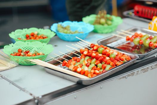 Colorful fruit skewers with strawberries and grapes at a vibrant outdoor market.