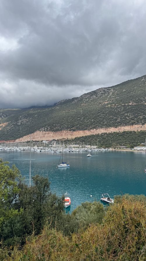 Free Tranquil bay in Kaş, Turkey featuring moored yachts and lush mountains under cloudy skies. Stock Photo