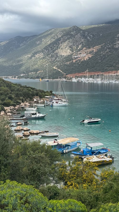 Free Serene bay with boats and dramatic mountains under a cloudy sky. Stock Photo