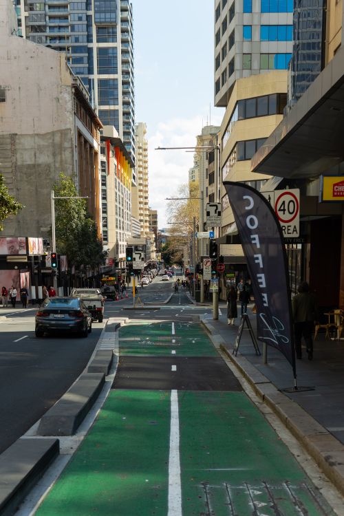 Free Bustling city street with a green bike lane, coffee shop, and high-rise buildings. Stock Photo