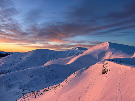 Captivating view of snow-covered mountains bathed in pink sunset light, with a vibrant sky above.