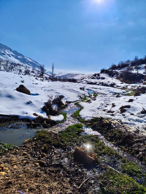 Free A pristine snowy landscape featuring a shimmering stream in Bloudan, Syria, under a clear blue sky. Stock Photo