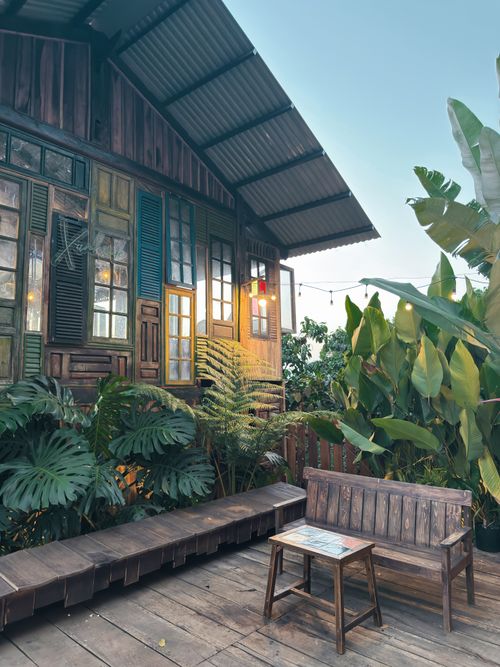 Free Charming rustic house exterior with vibrant plants and wooden furniture in a serene setting. Stock Photo