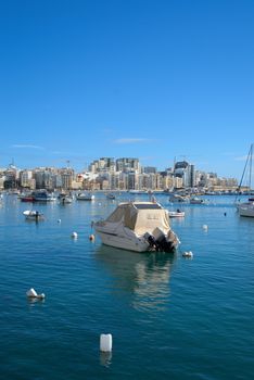 Serene scene of boats anchored in Sliema harbor with Malta's skyline in the background.