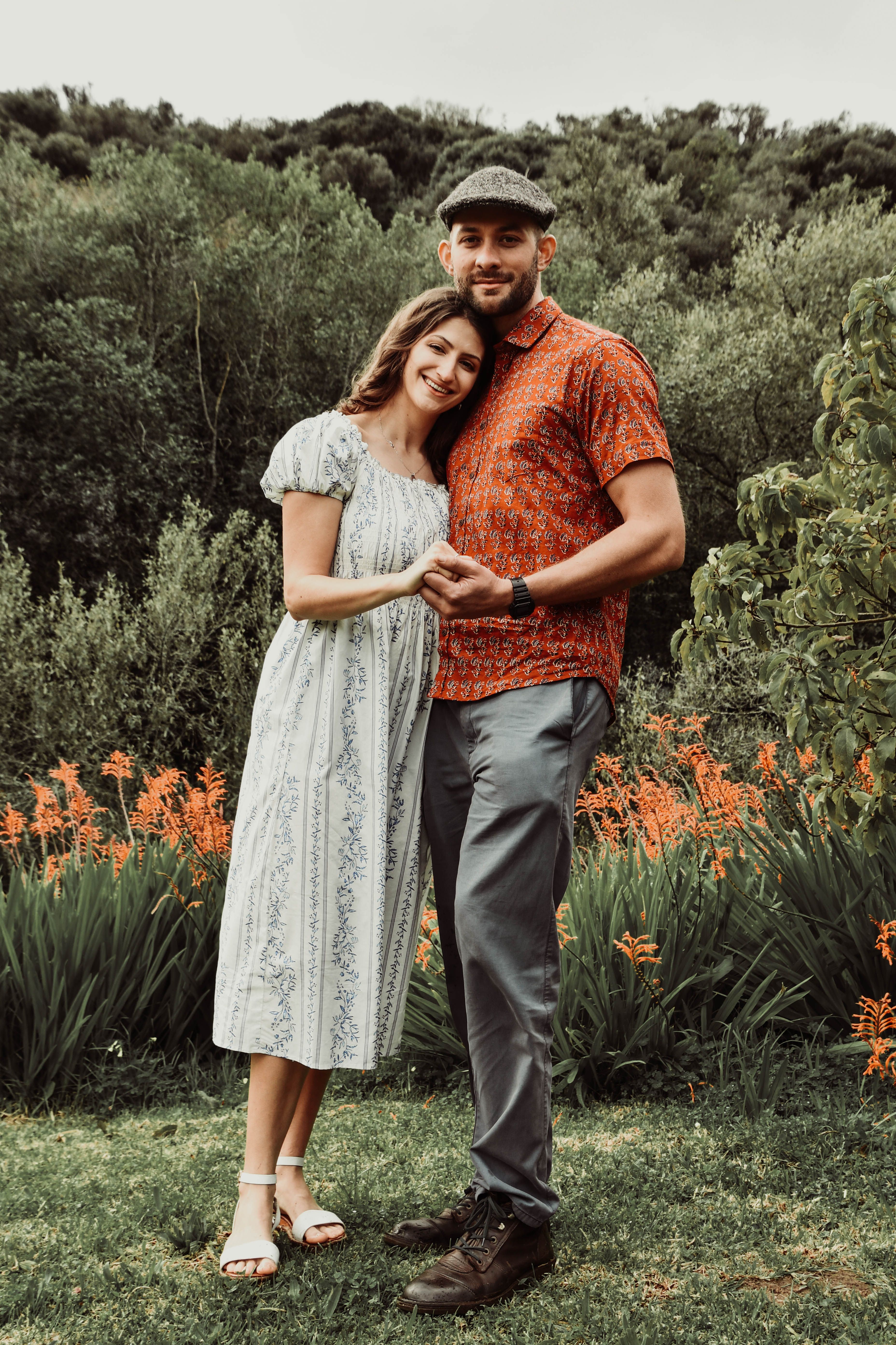 A joyful couple embraces in a scenic garden surrounded by lush greenery and vibrant flowers.