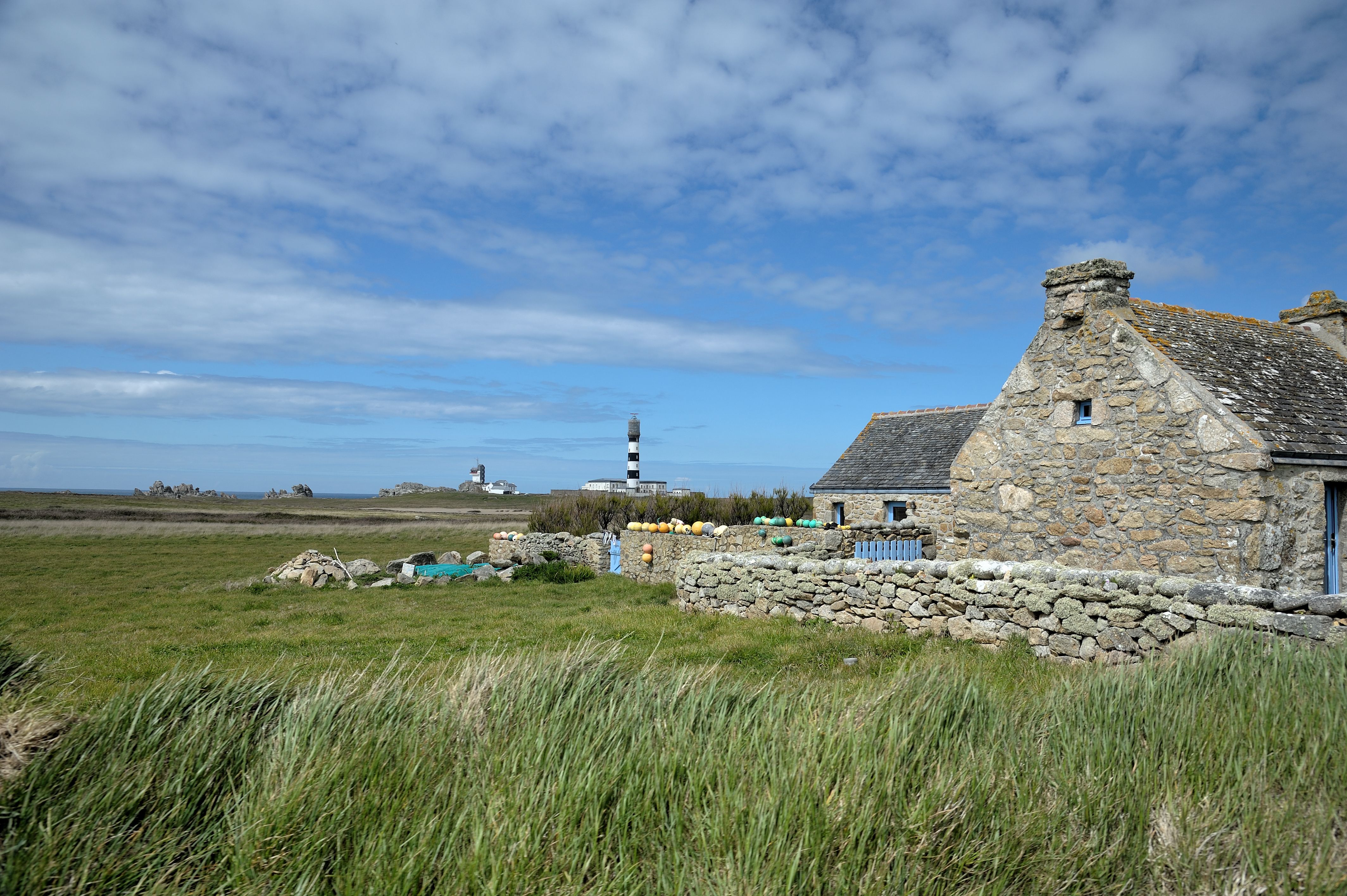 Charming stone cottage with a lighthouse view in Bretagne, France, under a blue sky.