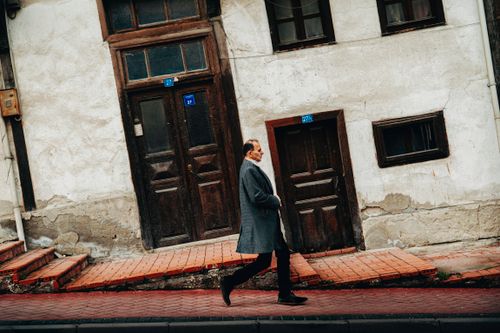 Free A man in a coat walks along the sidewalk near a worn city building. Stock Photo