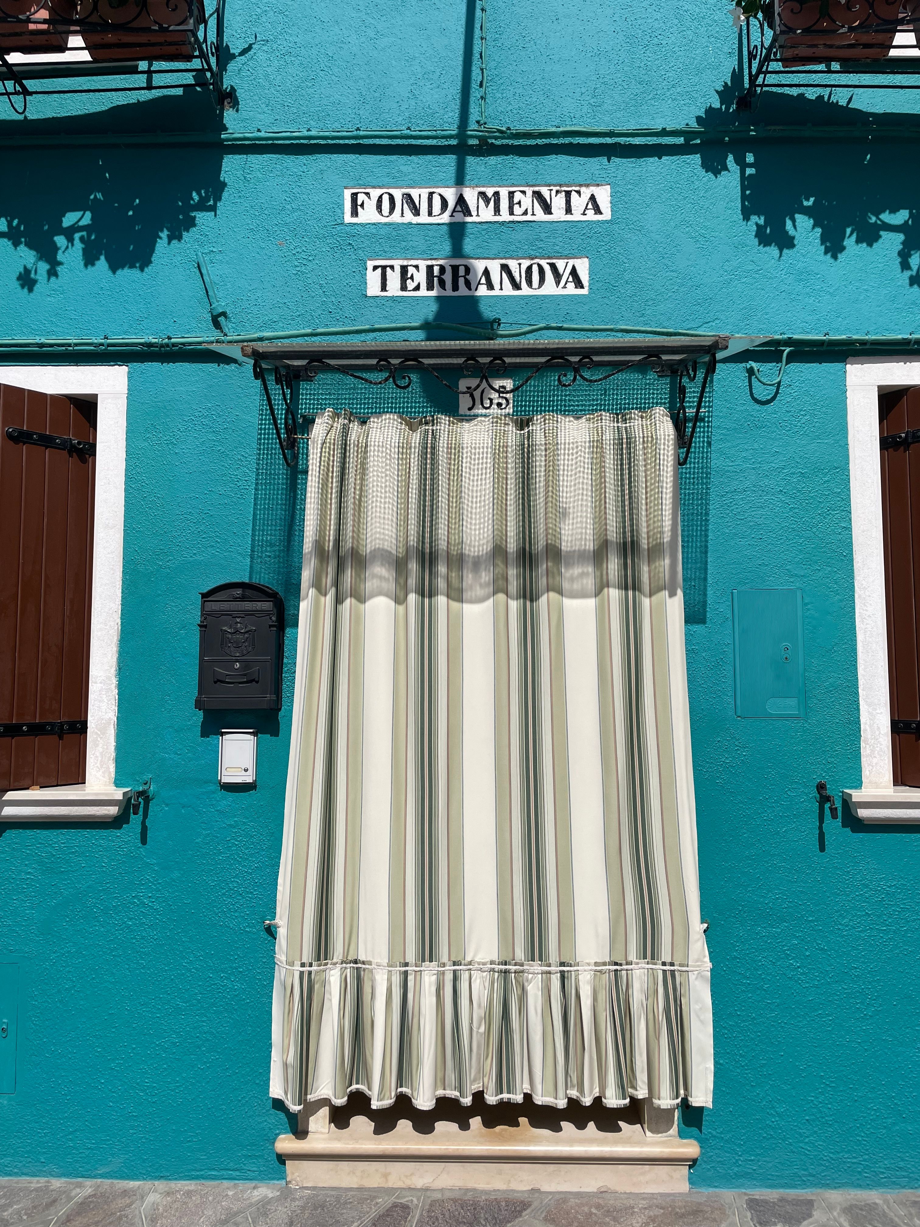 A picturesque facade on Burano island with a vibrant blue wall and striped curtains, capturing Italian charm.