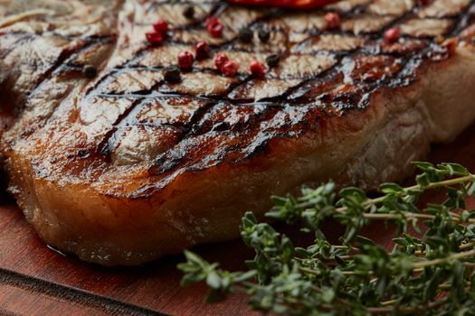 Close-up of succulent grilled ribeye steak with peppercorn and fresh thyme on a wooden board.