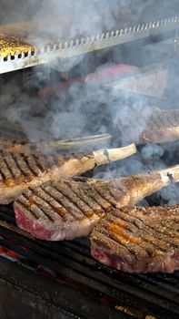 Grilled tomahawk steaks sizzling on a smoky barbecue grill, showcasing perfect sear marks.