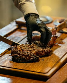 Black-gloved chef slicing a perfectly grilled tomahawk steak on wooden board.