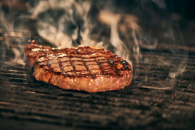 Thick steak with crosshatch grill marks searing over a smoky hot grill grate