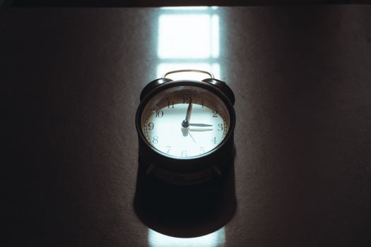 A vintage alarm clock in cozy morning light casting artistic shadows on a desk.