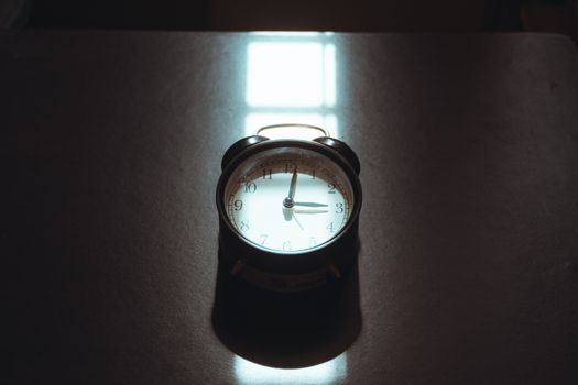A classic vintage alarm clock casting artistic shadows on a desk surface with moody lighting.
