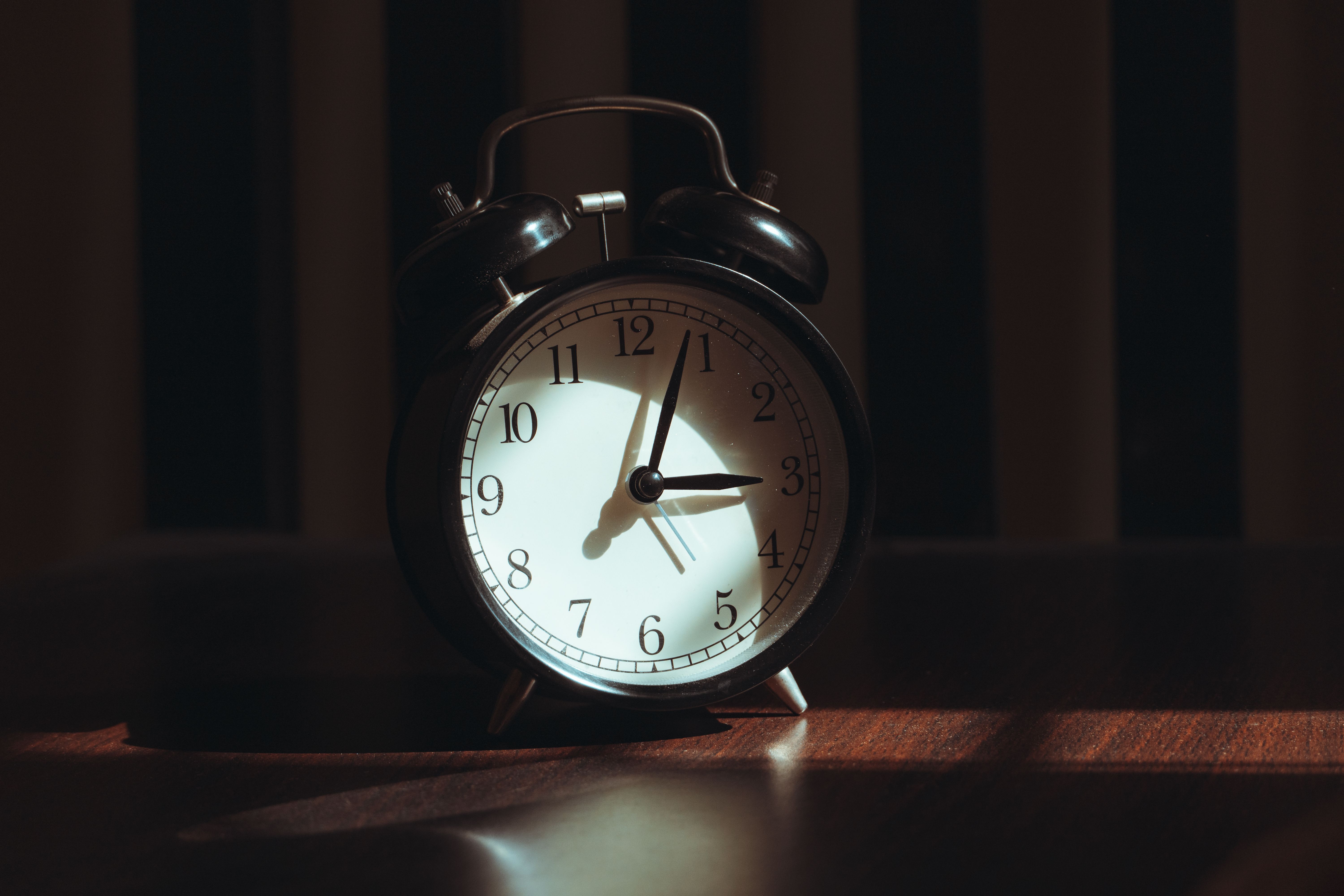 A classic black analog alarm clock illuminated by warm light and artistic shadows.