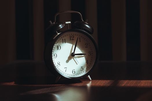 A classic black analog alarm clock illuminated by warm light and artistic shadows.