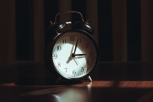 Free A classic black analog alarm clock illuminated by warm light and artistic shadows. Stock Photo