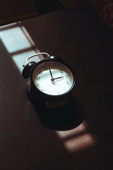 A vintage black analog clock on a wooden surface bathed in soft morning light, creating an artistic shadow play.