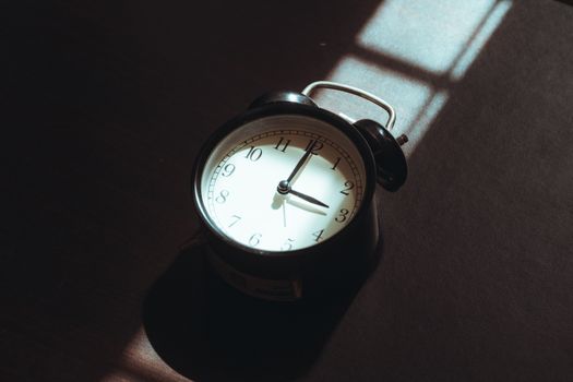 A vintage black alarm clock sits in shadow, casting an artistic play of light and dark indoors.