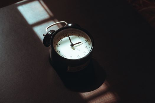 A classic black alarm clock casts shadows in warm morning light, evoking nostalgia.