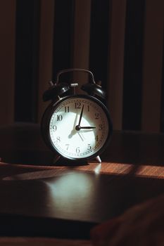 A black vintage alarm clock casting artistic shadows on a wooden surface, evoking nostalgia and tranquility.