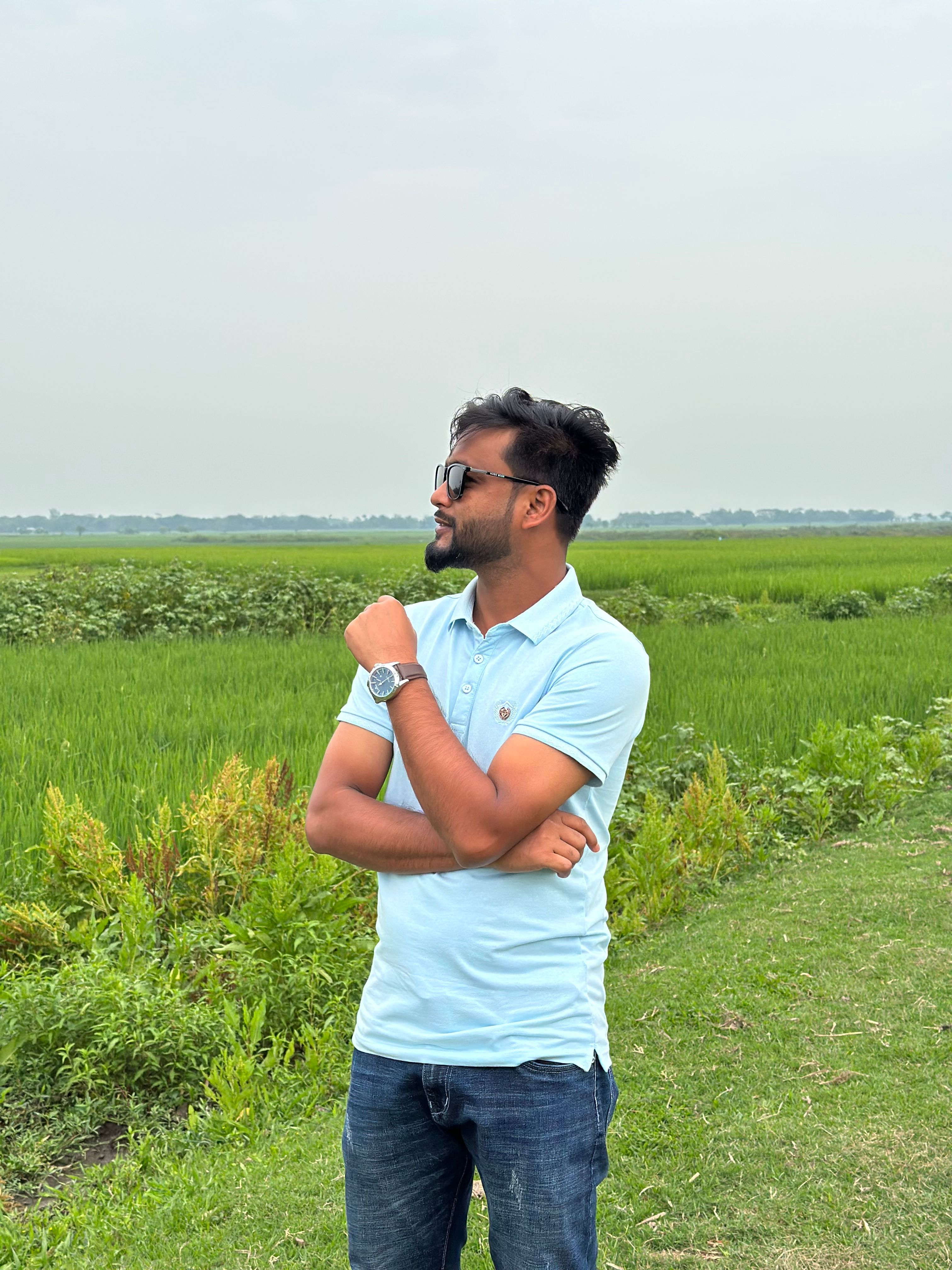 A man stands confidently in vibrant green fields in Atpara, Mymensingh, Bangladesh.