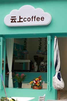 Open-air coffee shop with colorful signage, inviting decor and floral arrangement viewed through teal open windows.