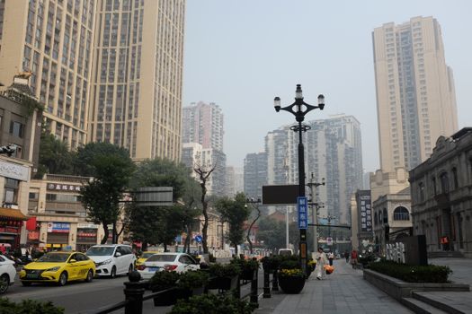Daytime view of a bustling urban street with high-rise buildings, trees, and traffic.