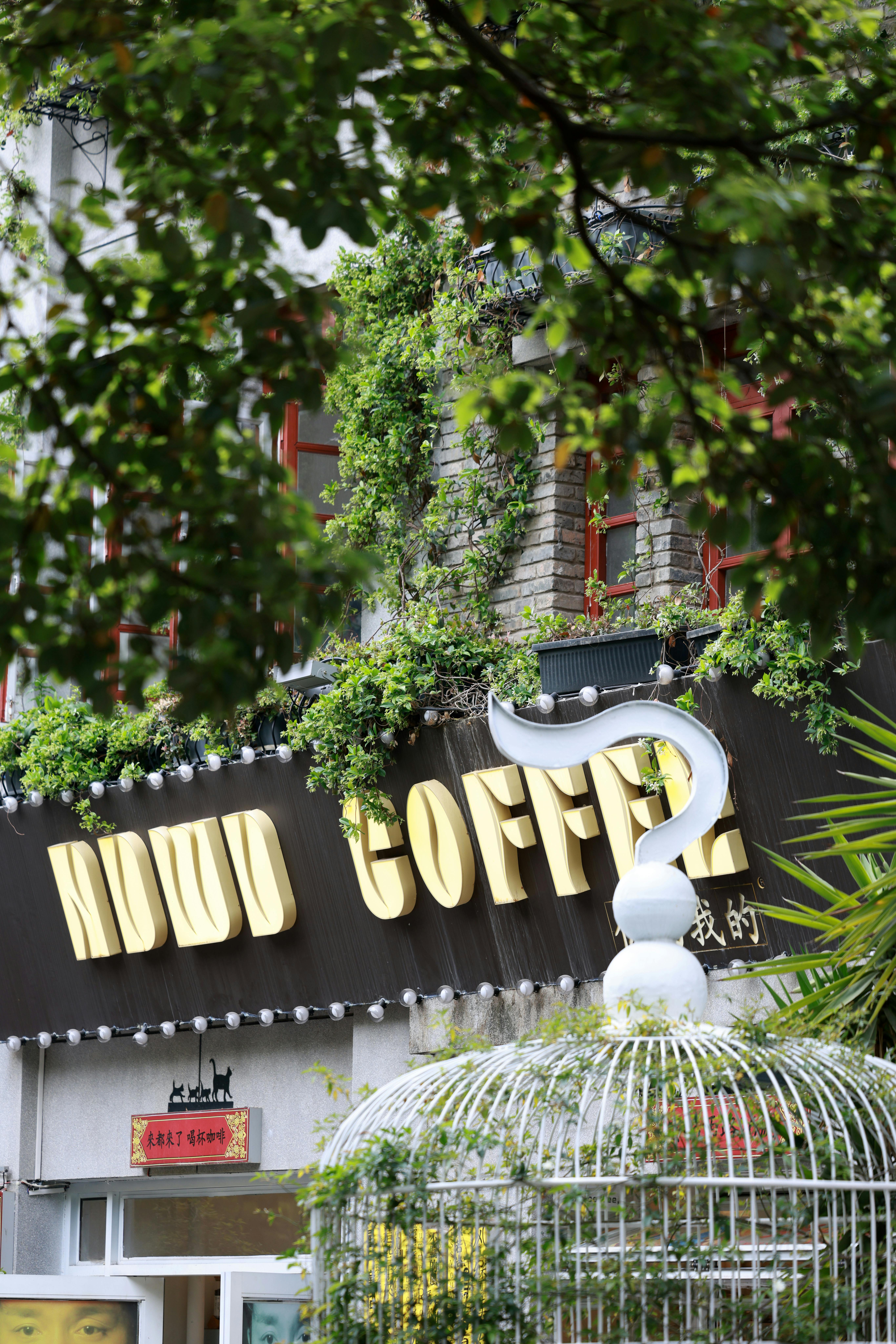 A charming outdoor coffee shop with lush greenery and a distinctive question mark sign, inviting ambiance.