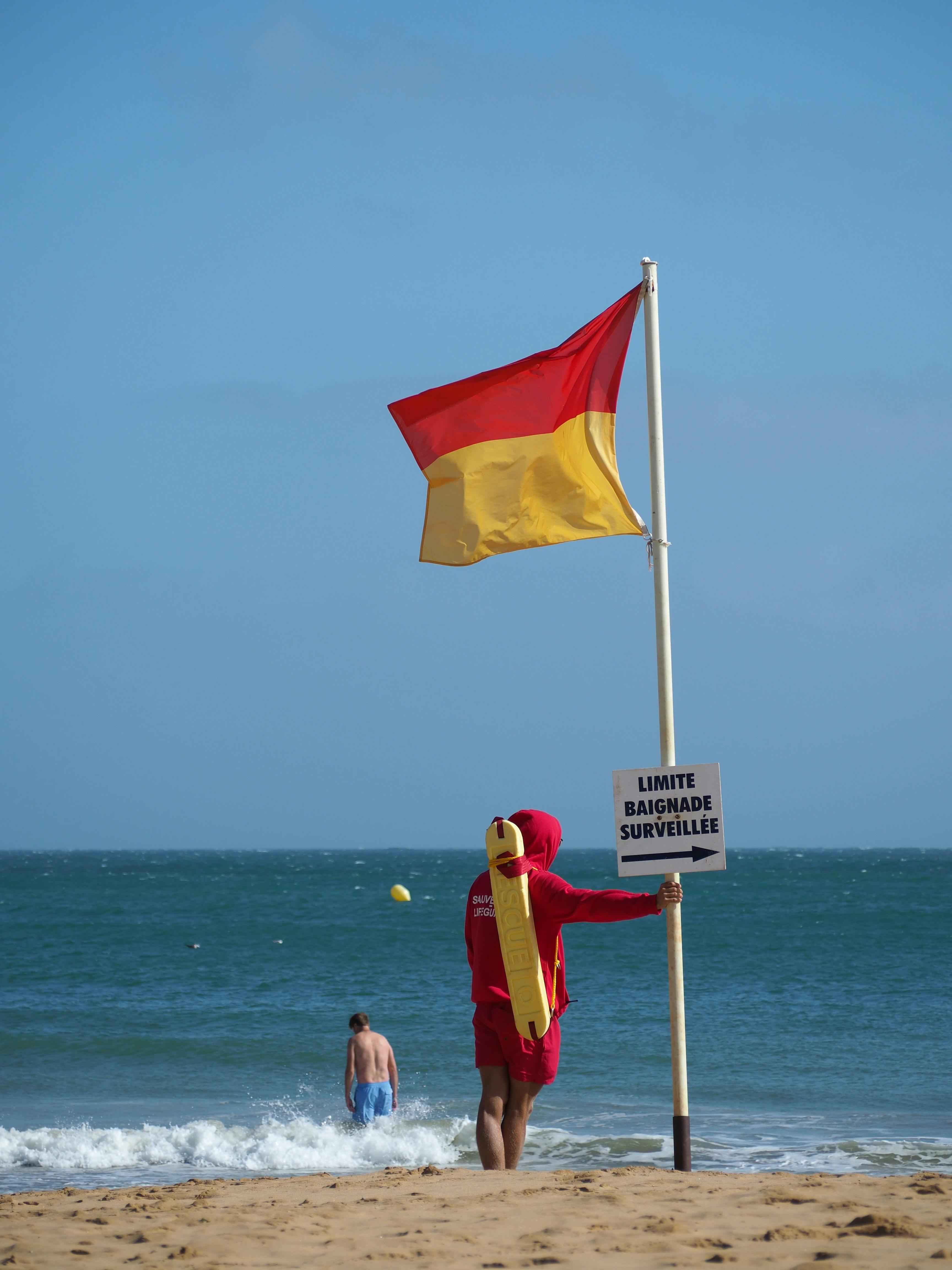 Lifeguard standing by a safety flag on a sunny beach, ensuring safety.