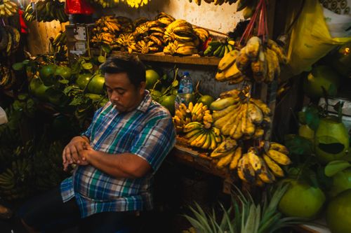 Free A man rests at a vibrant fruit stall in Jakarta, showcasing bananas and tropical fruits. Stock Photo