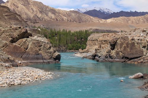 Free Peaceful river flowing through rocky valley with mountains in the background, ideal for nature themes. Stock Photo
