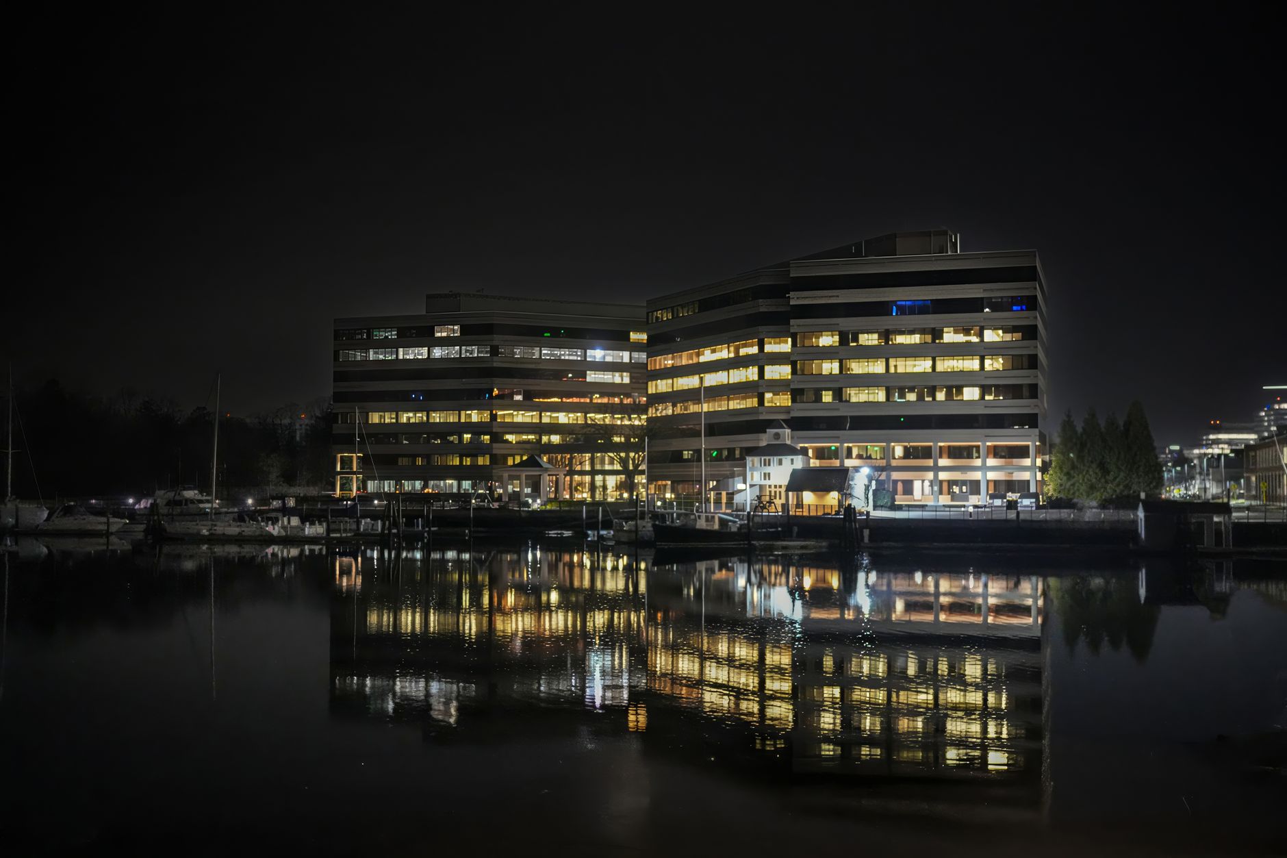 Office buildings illuminated at night reflecting on calm water, creating a dramatic cityscape scene.