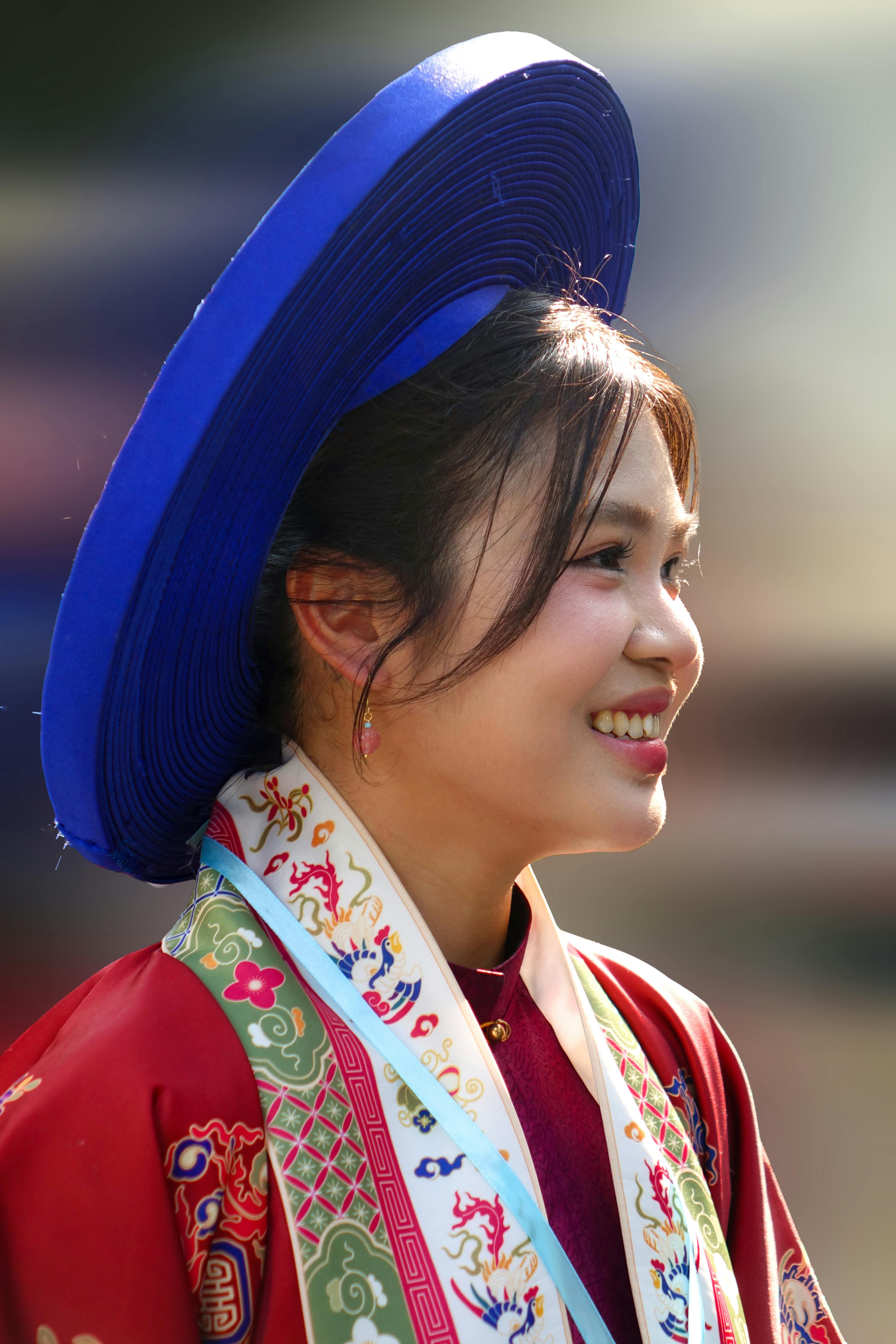Portrait of a smiling woman in traditional Vietnamese attire with a blue non la hat.