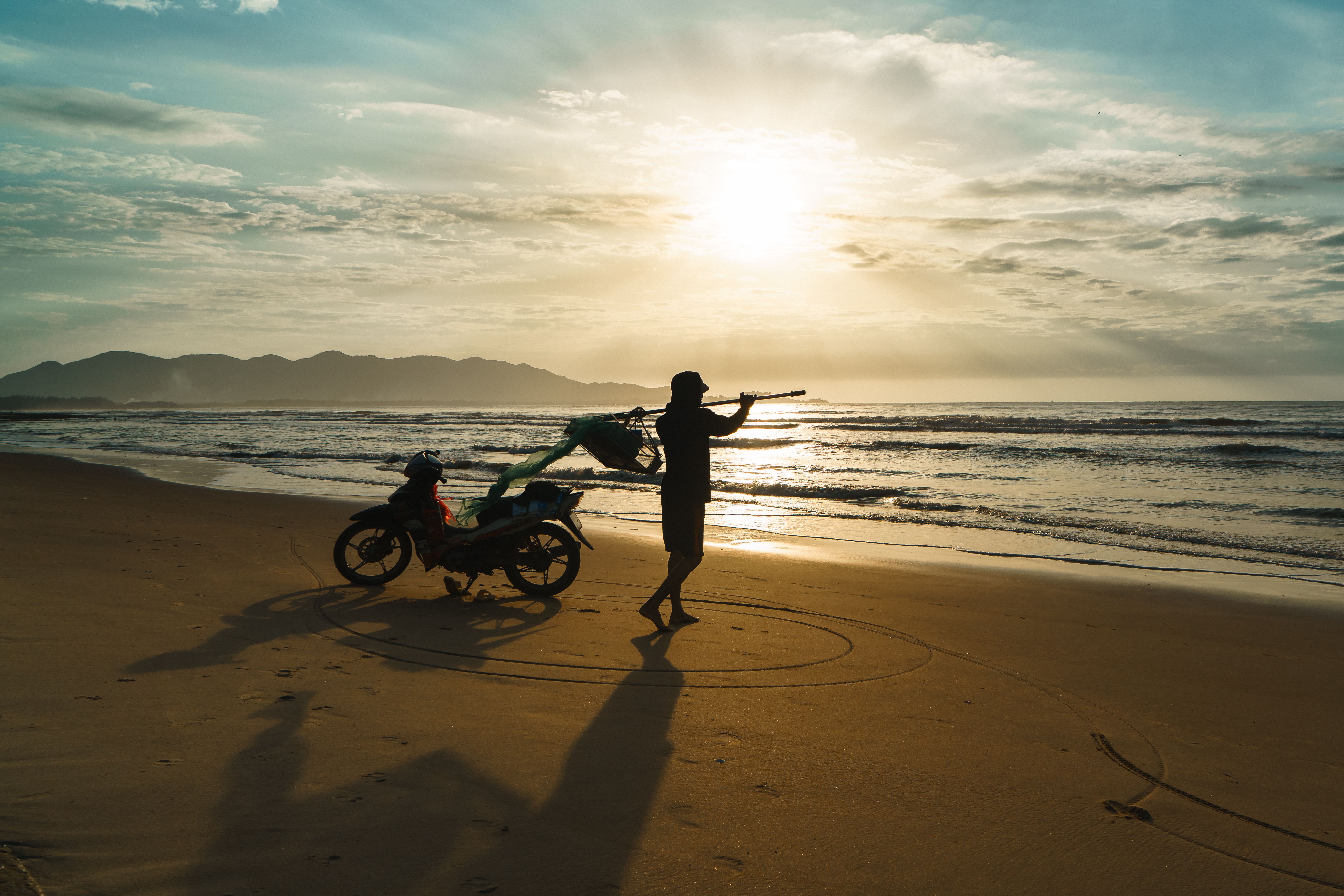 Silhouette of a fisherman with a motorcycle on Vũng Tàu Beach at sunrise, capturing daily life in Vietnam.